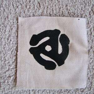 May include: A white fabric patch with a black vinyl record symbol printed on it.