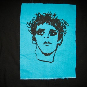 May include: A black and white line drawing of a person's face on a light blue fabric patch.