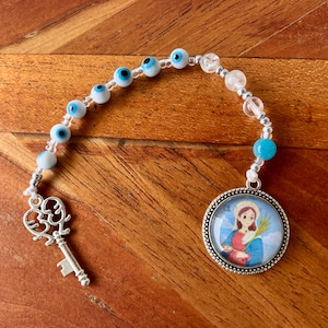 May include: A beaded religious charm with blue evil eye beads, clear crystal beads, and a turquoise bead. It features a silver-colored key charm and a round pendant with a religious image.