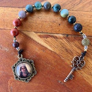 May include: A beaded rosary with a religious pendant and a decorative key charm. The rosary beads are in various colours, including red, green, and brown. The pendant is in a bronze-coloured setting.