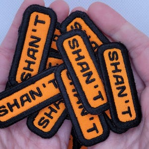 May include: A pile of orange and black fabric patches with the text "Shan-T" on each patch.
