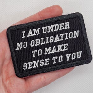 May include: Black embroidered patch with white text that reads "I am under no obligation to make sense to you".
