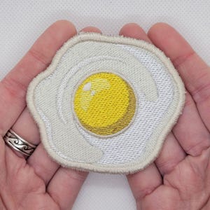 May include: White embroidered patch shaped like a fried egg with a yellow yolk.