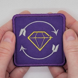 May include: Purple embroidered patch with a yellow diamond and silver arrows in a circular design.
