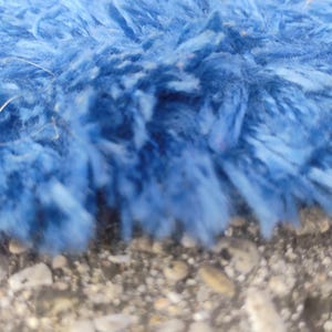 Puede incluir: Una vista de cerca de un material de tela azul brillante, peludo y texturizado. Las fibras son largas, suaves y densamente compactas, creando una apariencia de pelo largo con varios tonos de azul visibles en la superficie del material.
