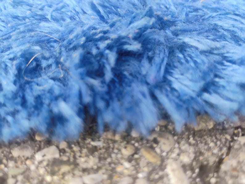 Puede incluir: Una vista de cerca de un material de tela azul brillante, peludo y texturizado. Las fibras son largas, suaves y densamente compactas, creando una apariencia de pelo largo con varios tonos de azul visibles en la superficie del material.