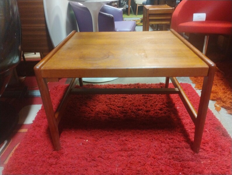 May include: A rectangular wooden coffee table with a light brown finish and a simple design. The table has a lower shelf and sits on a red shag rug.