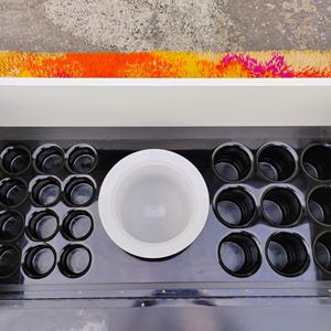 May include: A black bar cart with a white top and a black interior. The interior has a large white bowl and 12 small black cups.