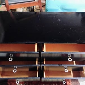 May include: A black dresser with six drawers, each with a white circular handle. The drawers are open, revealing a light brown interior. The top of the dresser is glossy black.