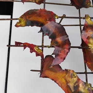 May include: Abstract metal wall art with a grid design. The metal pieces are painted in shades of red, orange, and gold.