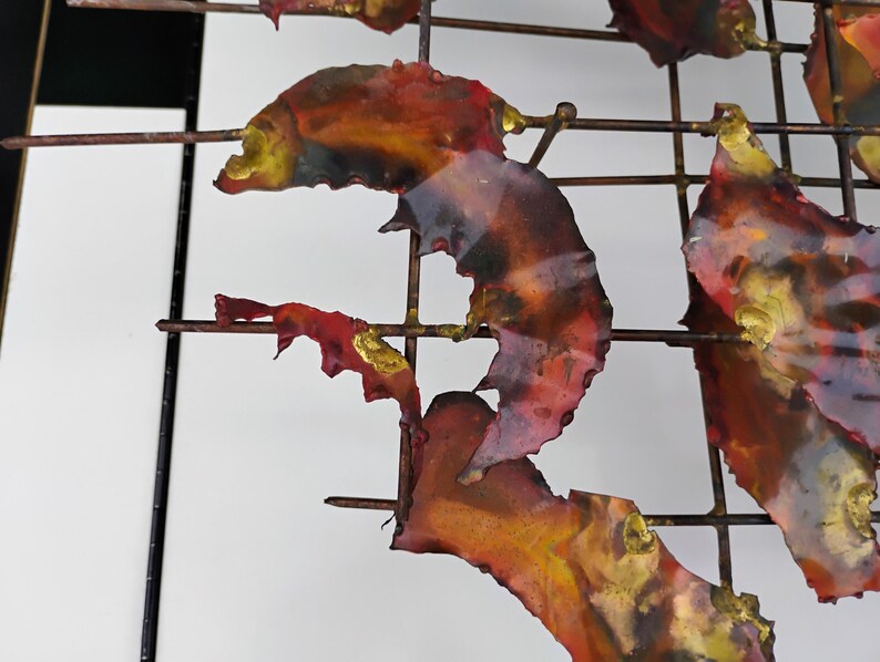May include: Abstract metal wall art with a grid design. The metal pieces are painted in shades of red, orange, and gold.