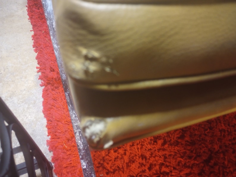 K&ouml;nnte beinhalten: Nahaufnahme eines braunen Ledersofas mit einigen Abnutzungserscheinungen am Stoff. Das Sofa steht auf einem roten Shaggy-Teppich.