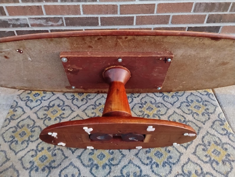 May include: A vintage, oval-shaped wooden table with a dark brown finish. The table has a pedestal base and a light-colored underside. The table is approximately 48 inches long and 30 inches wide.