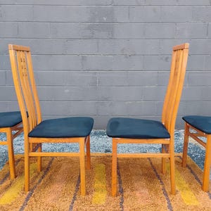 May include: A set of four wooden dining chairs with high, slatted backrests and dark blue upholstered seats. The chairs feature a light-toned wood frame with vertical slats in the backrest and straight legs, providing a simple, functional design.