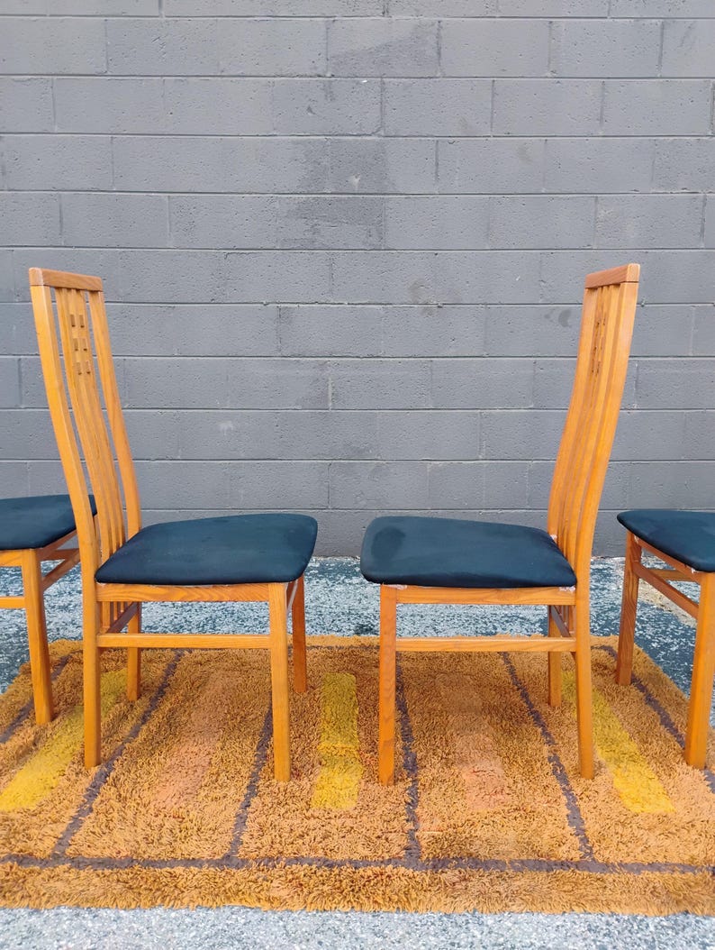 May include: A set of four wooden dining chairs with high, slatted backrests and dark blue upholstered seats. The chairs feature a light-toned wood frame with vertical slats in the backrest and straight legs, providing a simple, functional design.