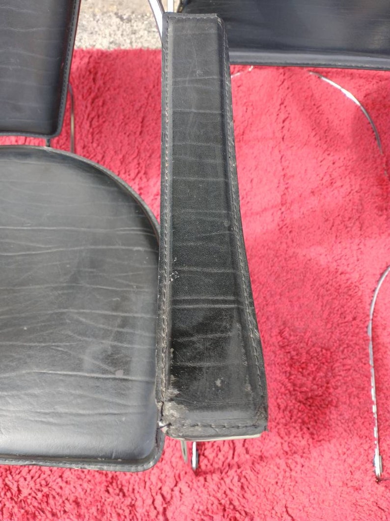 May include: Close-up of a black leather chair with chrome legs. The chair has a padded seat and back, and the leather is stitched with a diamond pattern.