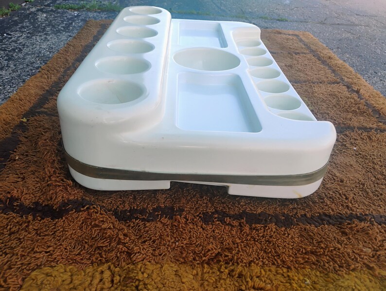 May include: A white plastic organizer tray featuring multiple circular indentations of varying sizes, two rectangular recessed compartments, and one central circular basin, all integrated into a single molded unit with a grey band around the base.
