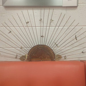 May include: A gold metal wall sculpture in the shape of a sun with birds flying around it.