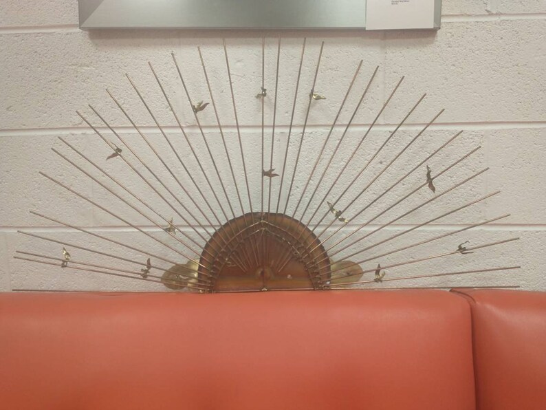 May include: A gold metal wall sculpture in the shape of a sun with birds flying around it.
