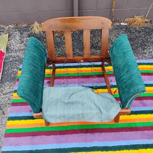 May include: A wooden chair frame featuring a curved backrest with three vertical slats, two upholstered armrests in a textured dark green fabric, and a matching seat cushion base with exposed metal coil springs visible in the center.
