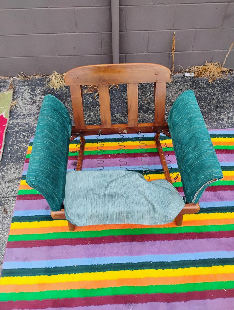 May include: A wooden chair frame featuring a curved backrest with three vertical slats, two upholstered armrests in a textured dark green fabric, and a matching seat cushion base with exposed metal coil springs visible in the center.
