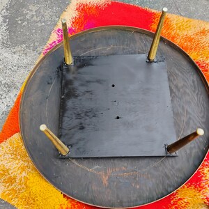 Op de afbeelding: De onderkant van een ronde houten tafel met een zwart geverfd oppervlak en vier gouden metalen poten.