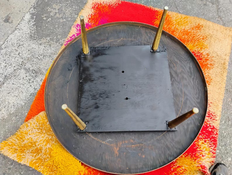 Op de afbeelding: De onderkant van een ronde houten tafel met een zwart geverfd oppervlak en vier gouden metalen poten.