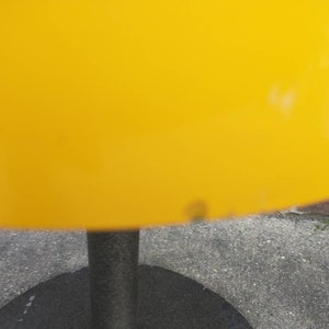 May include: A yellow lampshade with a black metal base. The lampshade is made of a smooth, shiny material.