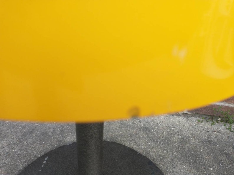 May include: A yellow lampshade with a black metal base. The lampshade is made of a smooth, shiny material.