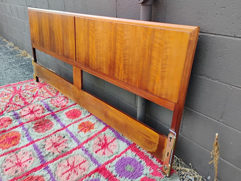 May include: A rectangular wooden headboard featuring a warm, medium-brown wood grain finish. The headboard is constructed with two large, smooth upper panels and a horizontal lower support rail, connected by vertical side posts with metal hardware.
