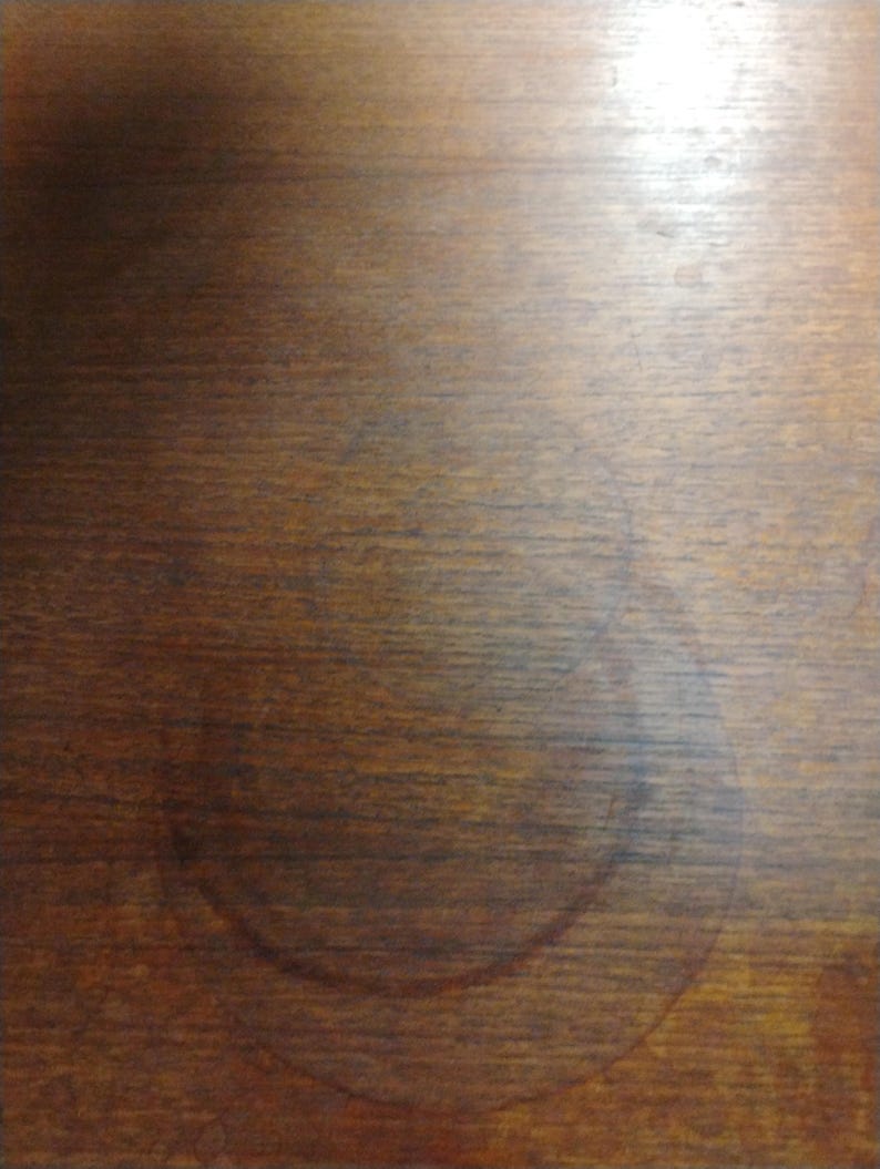 May include: A close-up of a dark brown wooden surface with a large, circular, light brown water stain.