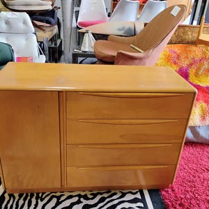 Op de afbeelding: Een licht houten dressoir met drie lades en een kastdeur. Het dressoir staat op een zebraprint tapijt.