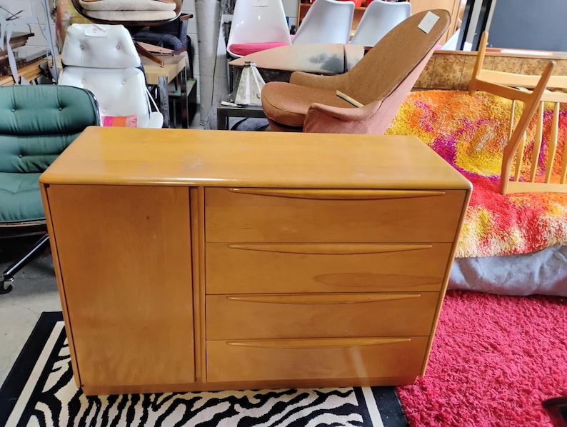 Op de afbeelding: Een licht houten dressoir met drie lades en een kastdeur. Het dressoir staat op een zebraprint tapijt.