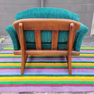 May include: An armchair featuring a wooden frame with a curved backrest and vertical slats. The seat and back cushions are upholstered in a textured, deep teal green fabric with subtle vertical white stripes throughout the material.