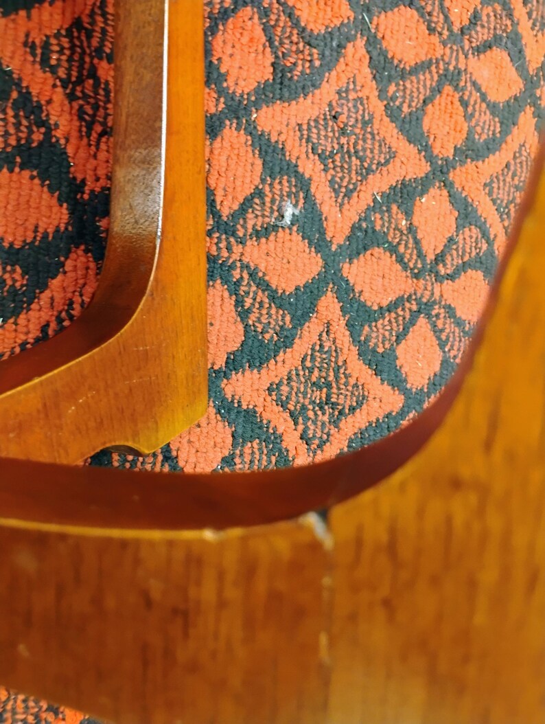 May include: A polished wooden chair frame with curved armrests and legs, featuring a smooth, light brown wood grain finish. The chair is upholstered in a textured fabric with a repeating geometric pattern in black and burnt orange colors.