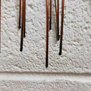 Puede incluir: Primer plano de una pared blanca con m&uacute;ltiples varillas met&aacute;licas delgadas y marrones que cuelgan hacia abajo. Las varillas est&aacute;n espaciadas uniformemente y parecen estar unidas a una superficie por encima de la pared.