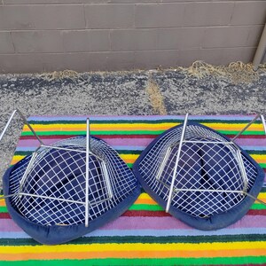 May include: Two chairs with dark blue fabric seats featuring a white grid pattern. Each chair has a silver-toned metal wire frame base. The chairs are positioned upside down, revealing the structural metal legs and the underside of the seats.