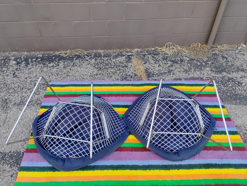 May include: Two chairs with dark blue fabric seats featuring a white grid pattern. Each chair has a silver-toned metal wire frame base. The chairs are positioned upside down, revealing the structural metal legs and the underside of the seats.