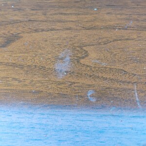 May include: A flat surface featuring a horizontal split design. The upper section displays a brown wood grain pattern with visible light-colored scratches and marks. The lower section is a solid, light blue color with a smooth, matte texture.