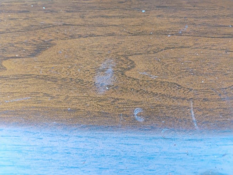May include: A flat surface featuring a horizontal split design. The upper section displays a brown wood grain pattern with visible light-colored scratches and marks. The lower section is a solid, light blue color with a smooth, matte texture.