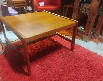 May include: A mid-century modern style coffee table with a wood top and a simple, sturdy frame. The table is sitting on a red shag rug.