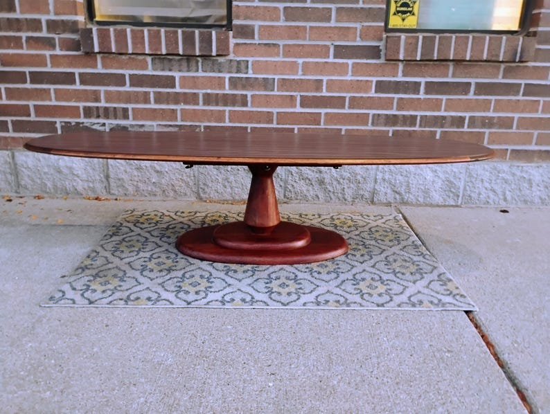 May include: A dark brown oval dining table with a pedestal base. The table is made of wood and sits on a patterned rug. The table is approximately 72 inches long.