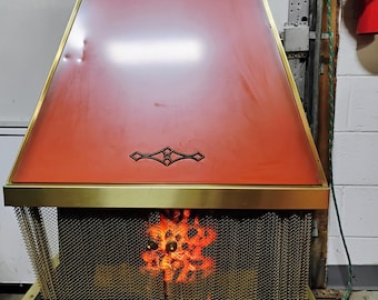 Könnte beinhalten: Ein elektrischer Kamin im Retro-Stil mit roter und goldener Oberfläche. Er hat einen Gitterrost und ein dekoratives Emblem. Das Innere leuchtet mit warmem, orangefarbenem Licht, das ein Feuer simuliert.