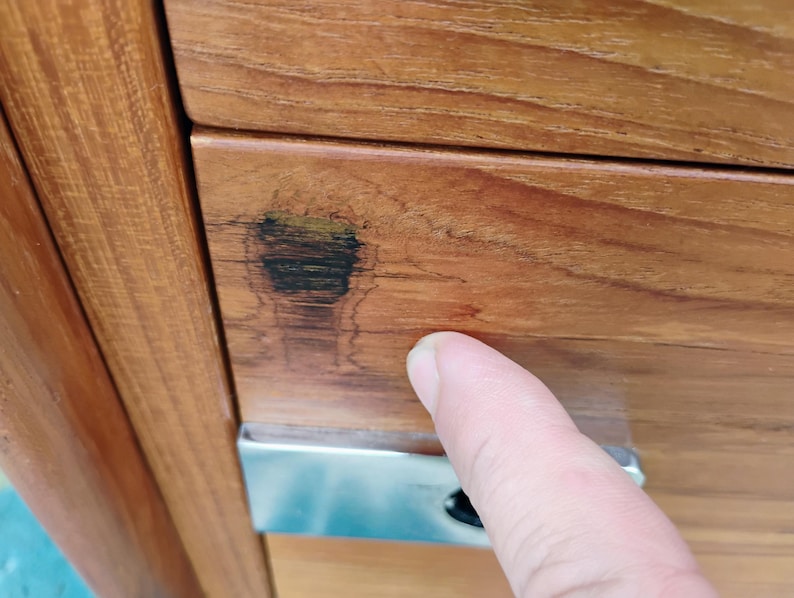 May include: A light brown wooden cabinet drawer featuring a prominent dark wood grain knot on the left side and a rectangular silver metal handle. The wood surface displays a smooth, polished finish with visible natural grain patterns throughout.