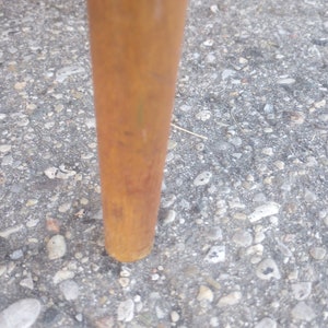 May include: Close-up of a wooden chair leg with a brown finish. The leg is resting on a gray gravel surface.