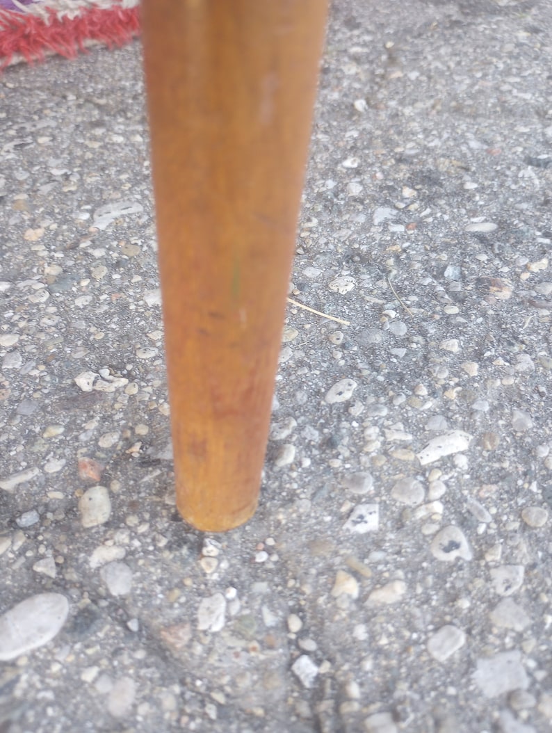 May include: Close-up of a wooden chair leg with a brown finish. The leg is resting on a gray gravel surface.