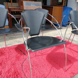 May include: Four black leather chairs with chrome frames. The chairs are arranged in a row on a red shag rug. The chairs have a unique design with a curved back and a wide seat.