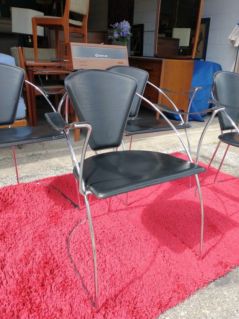 May include: Four black leather chairs with chrome frames. The chairs are arranged in a row on a red shag rug. The chairs have a unique design with a curved back and a wide seat.