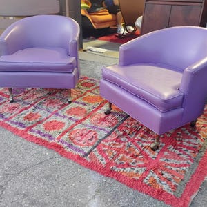 May include: Two purple chairs with a red and white patterned rug underneath. The chairs have a rounded back and a tufted seat.