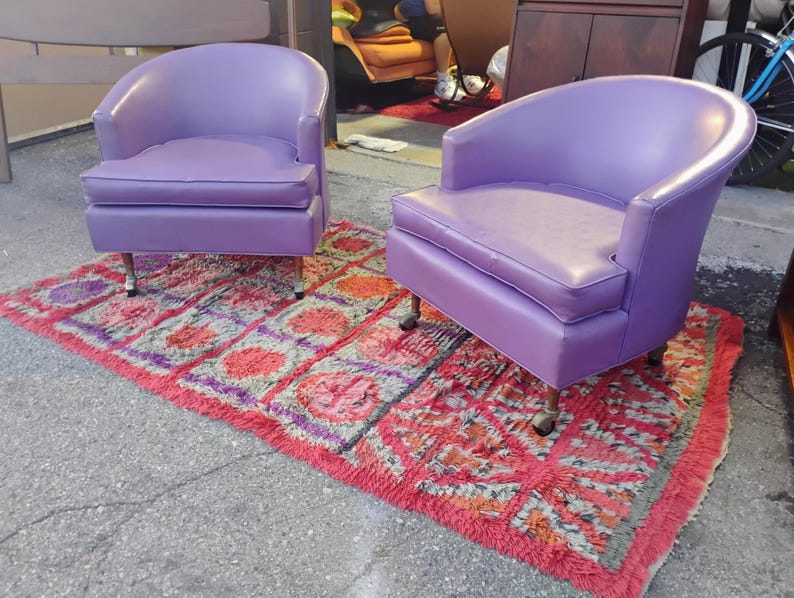 May include: Two purple chairs with a red and white patterned rug underneath. The chairs have a rounded back and a tufted seat.